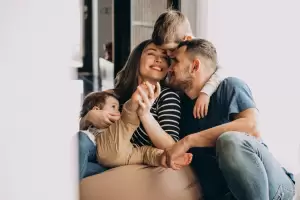 Familia feliz: madre, padre y dos niños pequeños abrazándose y sonriendo. Refleja la importancia de los seguros de vida para proteger el futuro familiar y considerar su tributación.