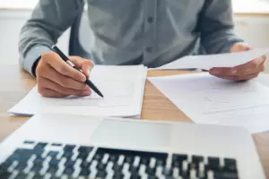 Un profesional de asesoría legal y fiscal revisando documentos con un bolígrafo, ilustrando el proceso de preparación de la declaración de la renta. La imagen transmite confianza en la asesoría experta para resolver las dudas sobre si tengo que hacer la declaración de la renta.