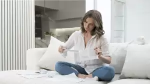 Una mujer revisa ansiosamente documentos de su vivienda en busca de cargas o gravámenes. La imagen representa la duda sobre cómo saber si una propiedad está libre de cargas.