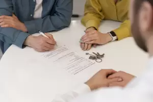 Vista de cerca de una pareja firmando un contrato de compraventa de vivienda. El asesoramiento profesional es clave para asegurar un certificado libre de cargas.