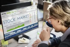 Hombre tomando café mientras revisa en el ordenador cómo tributa la venta de acciones en España 
