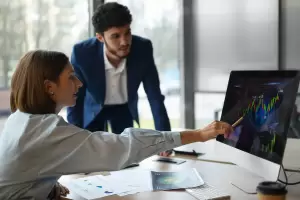 Mujer explicando a un hombre en el ordenador cómo tributa la venta de acciones en España mediante gráficos financieros 