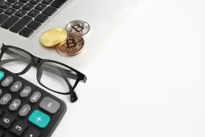 Digital currencies alongside a calculator and glasses, highlighting the detailed work involved in crypto tax reporting.