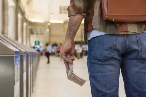 A back view of a person with a backpack, holding a travel ticket or document, walking towards a train station. The image represents the journey and procedures of an expat or digital nomad affected by tax regulations in Spain.