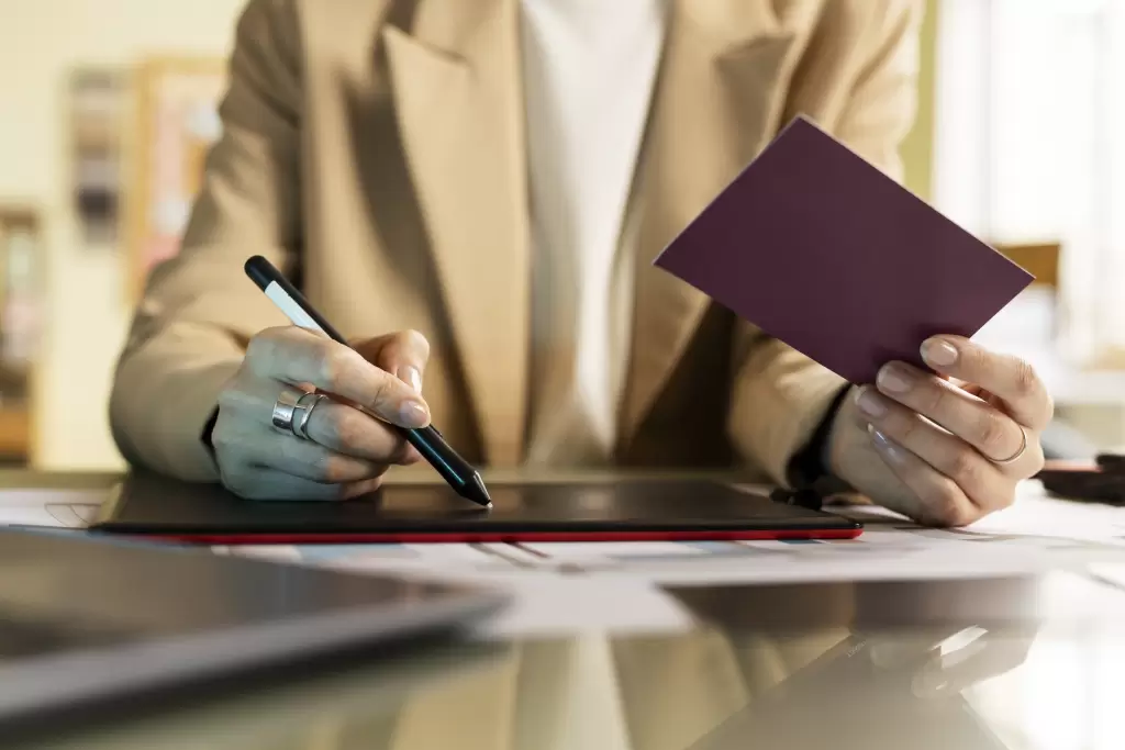 A person holding a passport in one hand and a stylus in the other, working on a digital tablet. The image symbolizes a non-resident handling their tax declarations and legal paperwork in Spain remotely.