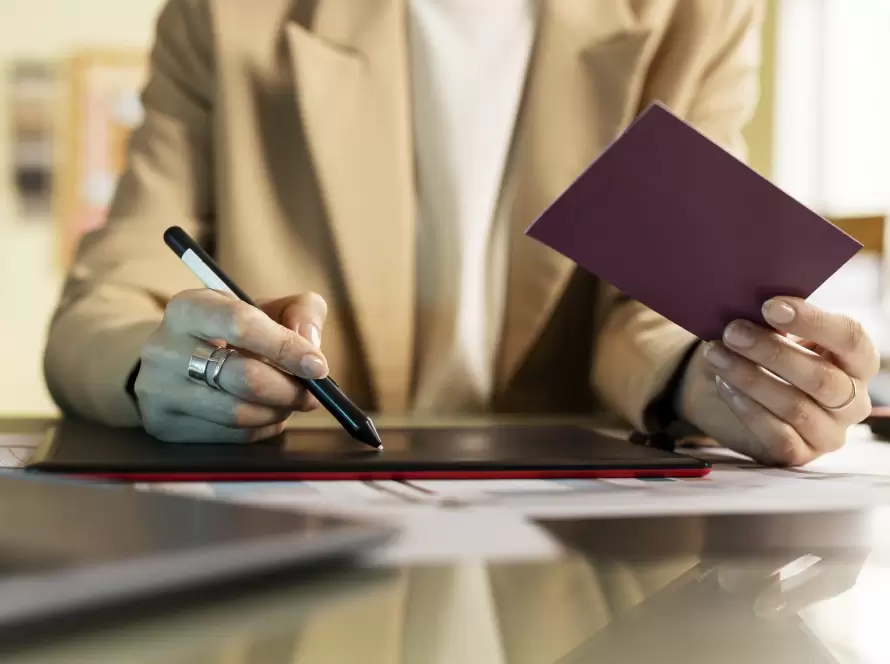 A person holding a passport in one hand and a stylus in the other, working on a digital tablet. The image symbolizes a non-resident handling their tax declarations and legal paperwork in Spain remotely.
