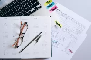 A flat-lay view of a calendar with highlighted dates, a pair of glasses, a pen, and tax forms, including a 1040 form. The image emphasizes the deadlines and necessary documentation for filing non-resident tax in Spain.