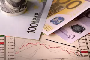 A close-up of different banknotes, including euros, on top of a financial chart with a downward-pointing arrow. The image represents the financial implications and tax considerations for non-residents in Spain.