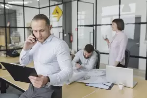 A male executive on the phone while reviewing a clipboard in a busy office environment, representing complex decisions for Beckham Law for Directors.
