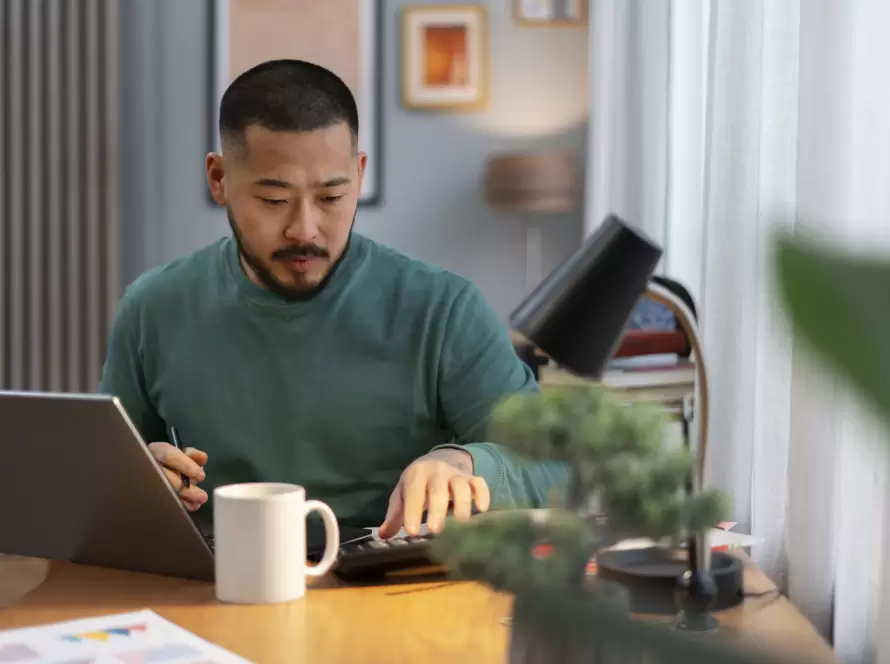 A man calculating expenses and working on a laptop from home, symbolizing financial considerations for Beckham Law for Remote Workers and digital nomads.